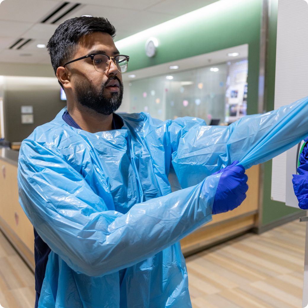 A nurse putting on a disposable blue gown and gloves in a hospital setting.