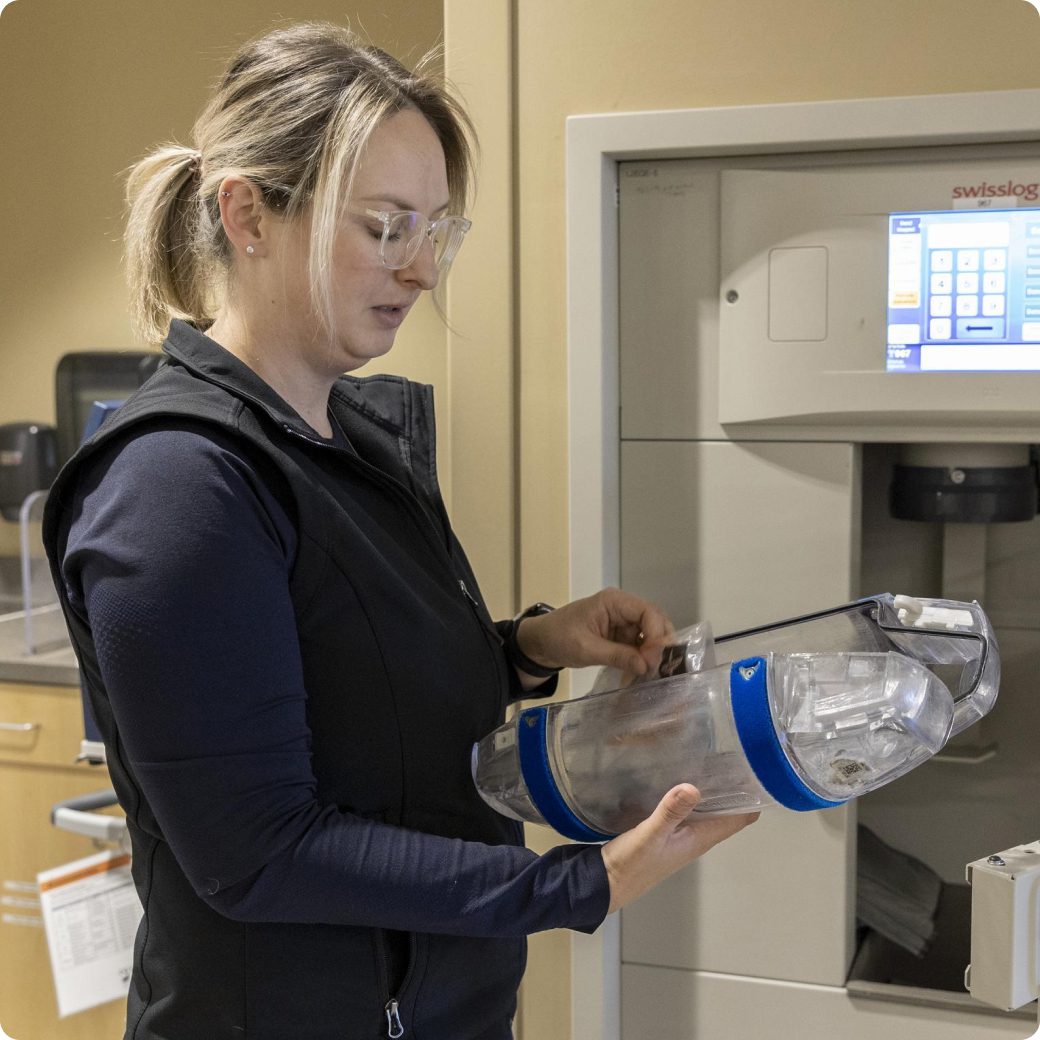  A nurse placing a clear, blue-capped pneumatic tube system carrier into a Swisslog station in the PACU.