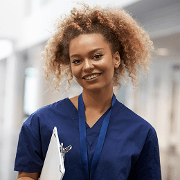  A female nurse in blue medical scrubs is smiling at the camera.