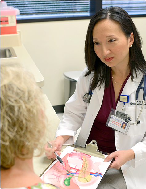 A doctor explaining an anatomical illustration on a clipboard to a patient in a medical exam room