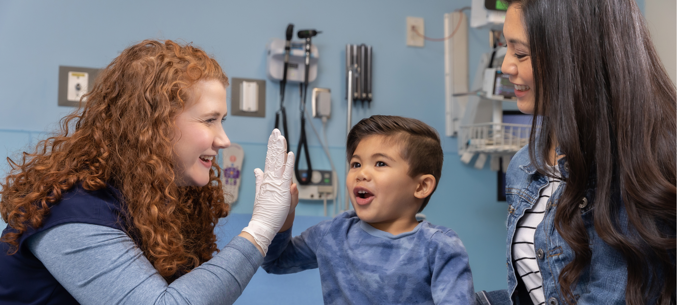 One female pediatric advanced practice provider (APP) high-fiving a boy sitting next to his mom