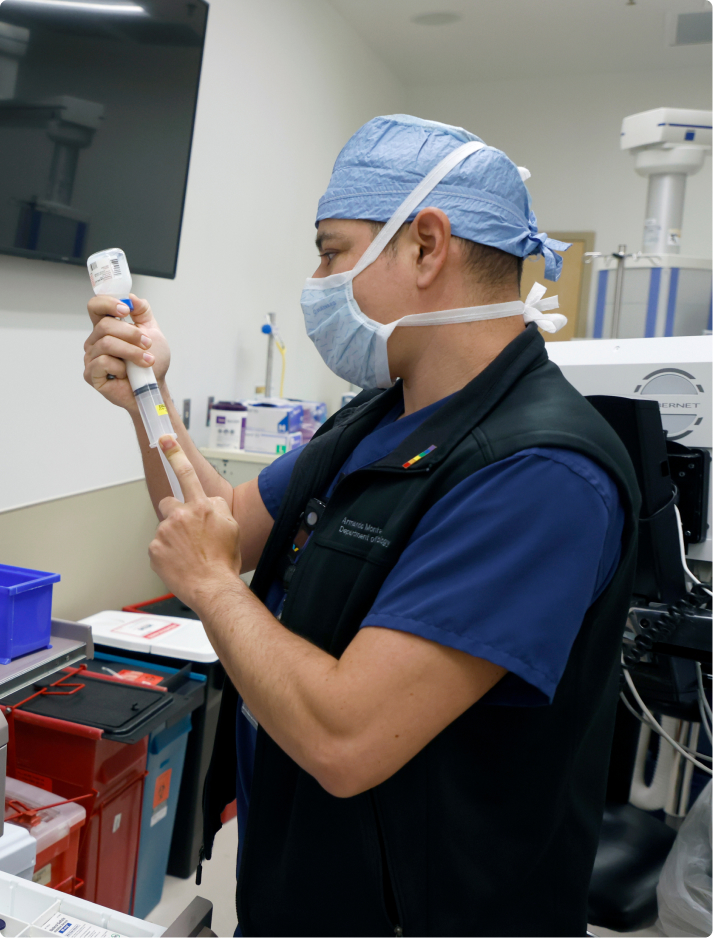 Male advanced practice provider (APP) CRNA with a mask fills syringe