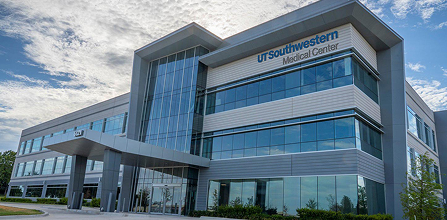 UT Southwestern Medical Center Las Colinas, a modern glass-front building with sleek design, set against a partly cloudy sky.
