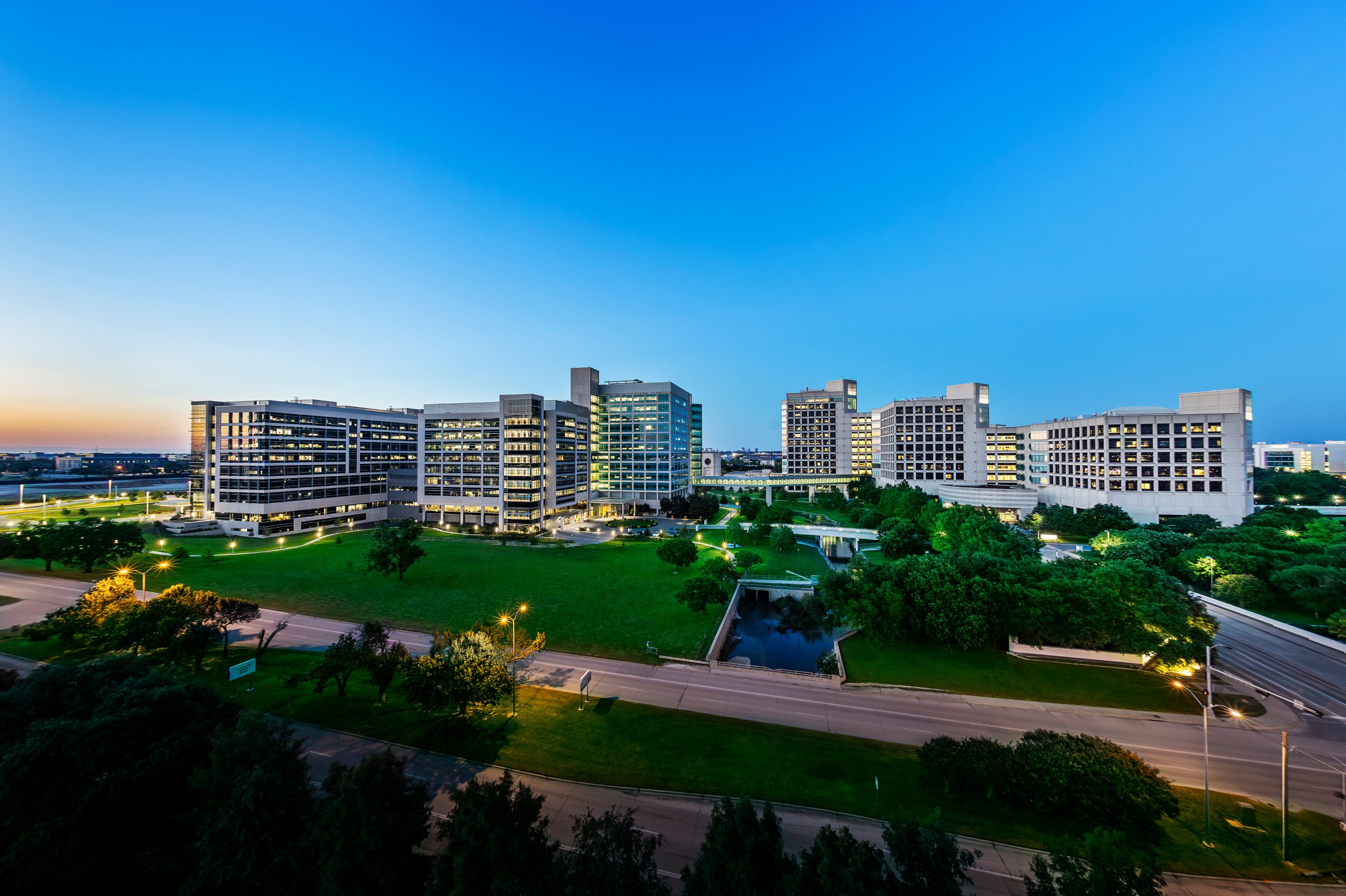 Aerial view of the UT Southwestern Medical Center campus at dusk, showing several large, medical and research buildings surrounding a large green lawn.